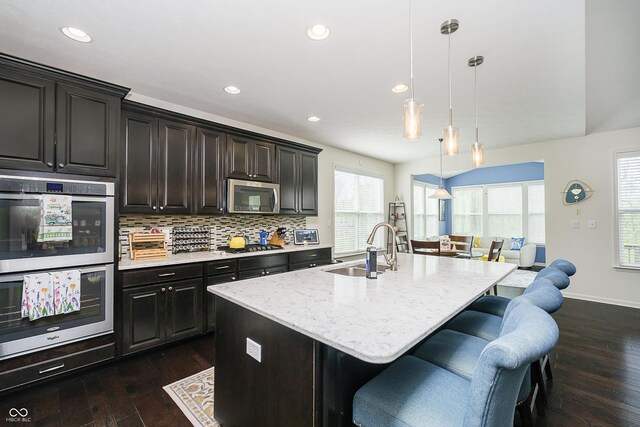 kitchen featuring a kitchen island with sink, tasteful backsplash, dark wood finished floors, a sink, and stainless steel appliances