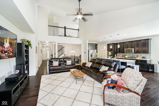 living room with stairs, dark wood-style flooring, a ceiling fan, and a towering ceiling