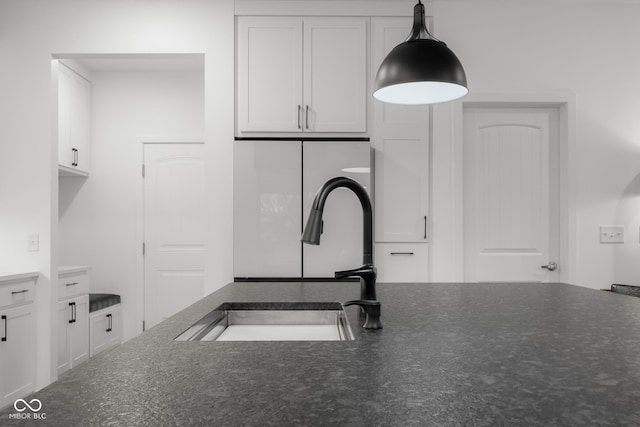 kitchen with a sink, hanging light fixtures, white cabinets, and dark stone counters