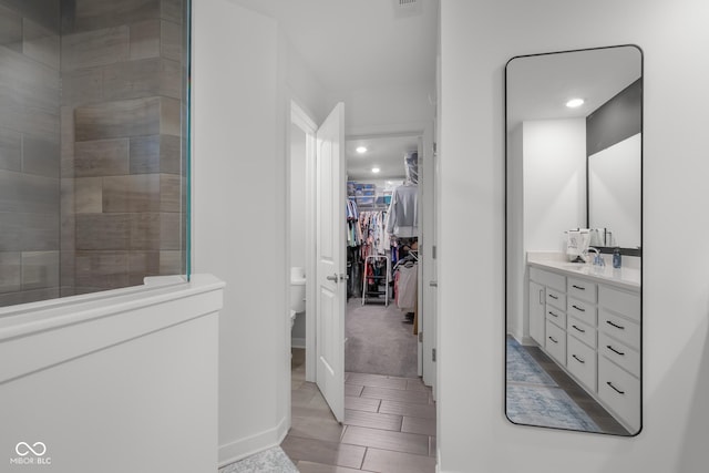 full bath featuring a walk in closet, vanity, tiled shower, and toilet