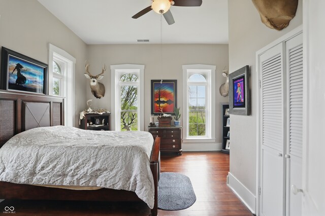 bedroom with a closet, wood finished floors, visible vents, a ceiling fan, and baseboards