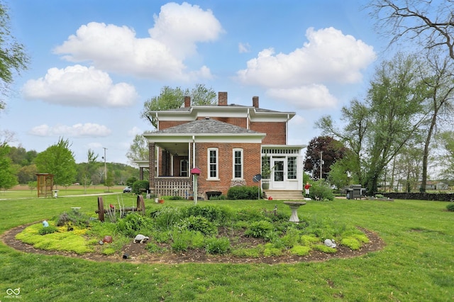 view of front facade featuring a chimney, a porch, brick siding, and a front lawn