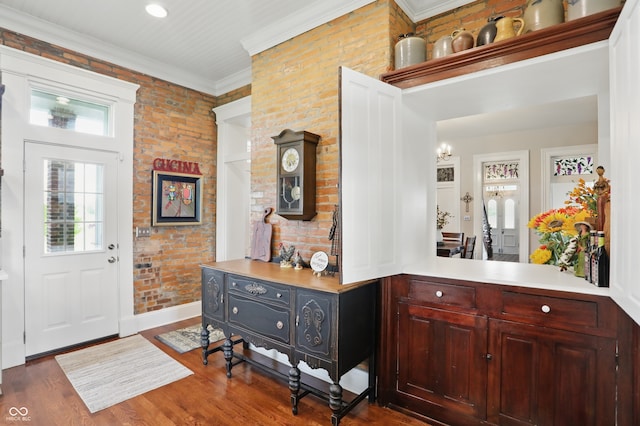 foyer entrance with a notable chandelier, brick wall, dark wood-type flooring, baseboards, and ornamental molding