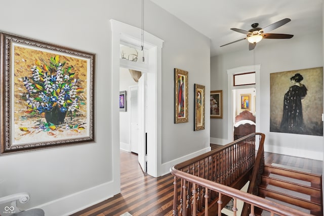 corridor with baseboards, an upstairs landing, and wood finished floors