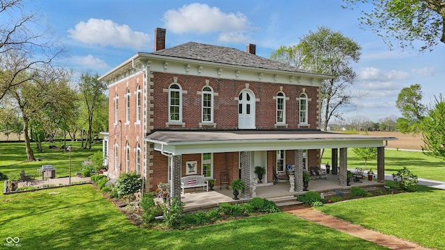 view of front of house with a porch, brick siding, a chimney, and a front yard