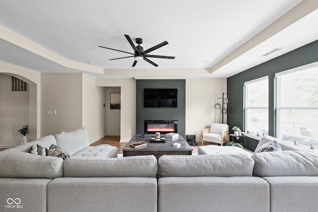 1024 Cyprian Way, Lebanon, IN 46052 - living room featuring a tray ceiling, ceiling fan, baseboards, a glass covered fireplace, and arched walkways
