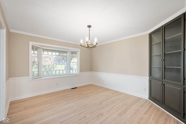 empty room featuring visible vents, light wood finished floors, ornamental molding, and an inviting chandelier