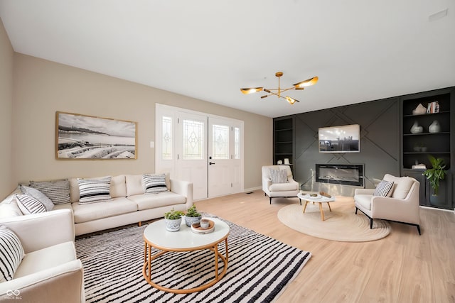 living room with built in features, baseboards, an inviting chandelier, a fireplace, and wood finished floors