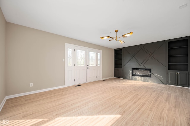 unfurnished living room featuring visible vents, baseboards, built in shelves, an inviting chandelier, and light wood finished floors