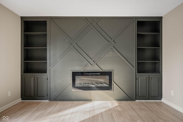 unfurnished living room with built in shelves, baseboards, and light wood finished floors