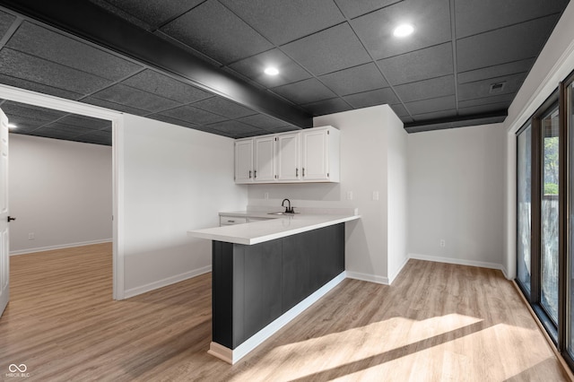 kitchen featuring a sink, white cabinets, a peninsula, and light wood-style floors