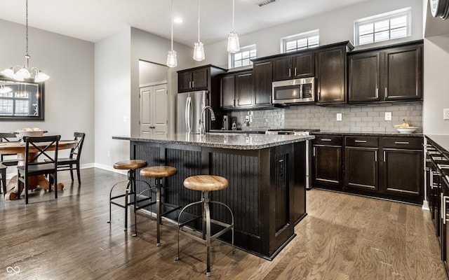 kitchen with a kitchen breakfast bar, appliances with stainless steel finishes, tasteful backsplash, dark stone counters, and an island with sink