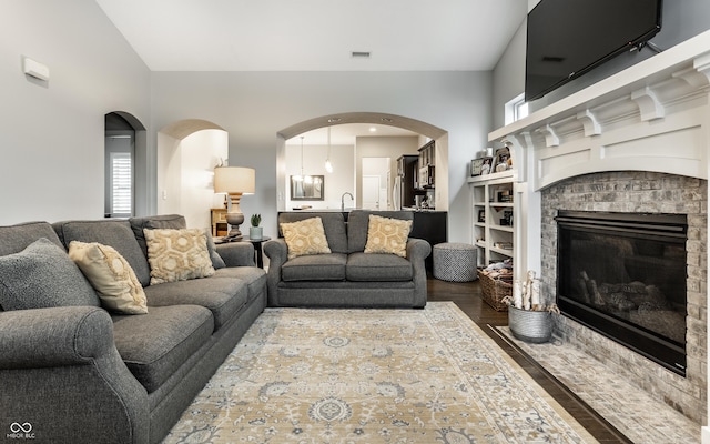 living room featuring visible vents, arched walkways, built in shelves, wood finished floors, and lofted ceiling