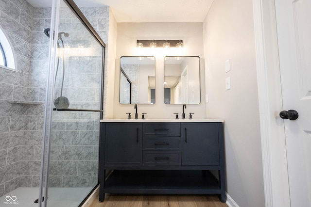 bathroom with a sink, a shower stall, double vanity, and wood finished floors