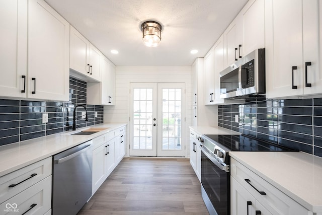 kitchen featuring white cabinetry, wood finished floors, a sink, stainless steel appliances, and french doors