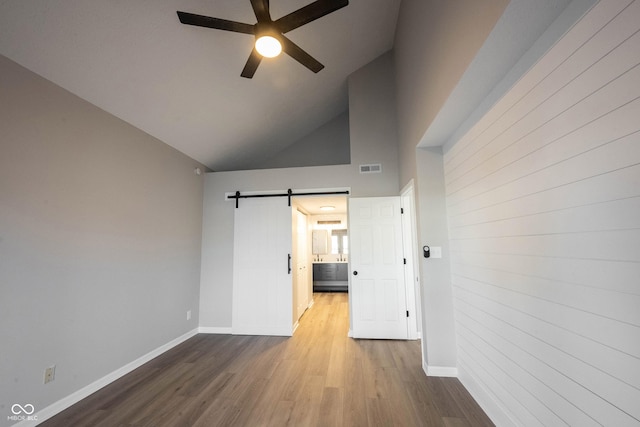 empty room featuring baseboards, a ceiling fan, a barn door, and wood finished floors