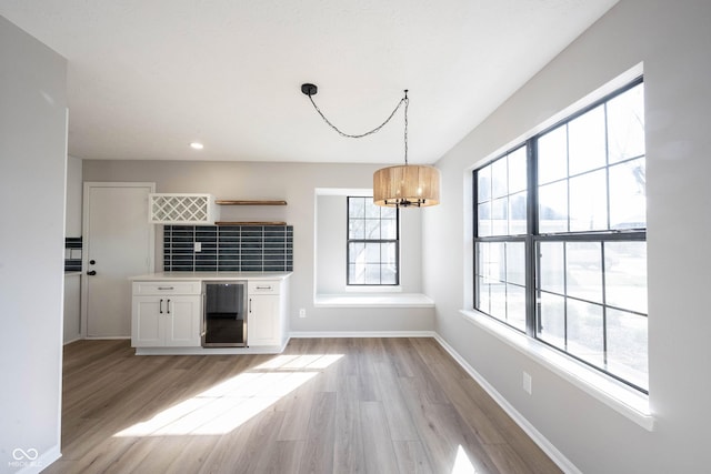interior space with a chandelier, light wood-style floors, beverage cooler, and baseboards