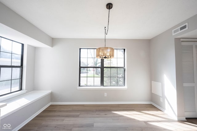 unfurnished dining area with visible vents, baseboards, an inviting chandelier, and wood finished floors