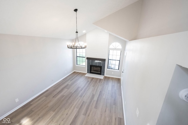 unfurnished living room featuring a notable chandelier, baseboards, a tiled fireplace, high vaulted ceiling, and light wood finished floors