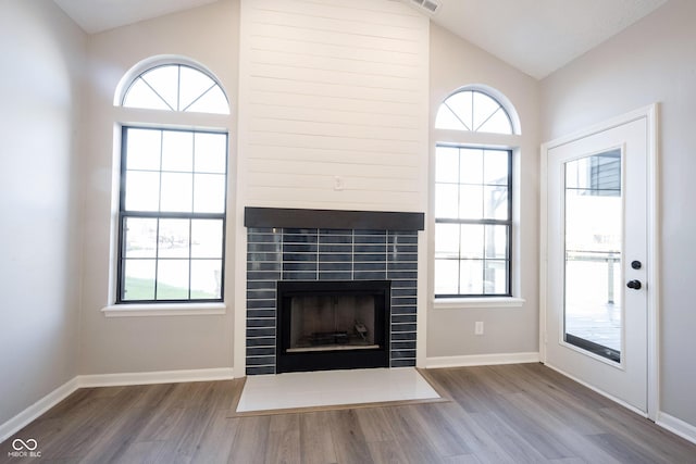 unfurnished living room featuring wood finished floors, a tiled fireplace, vaulted ceiling, and a wealth of natural light
