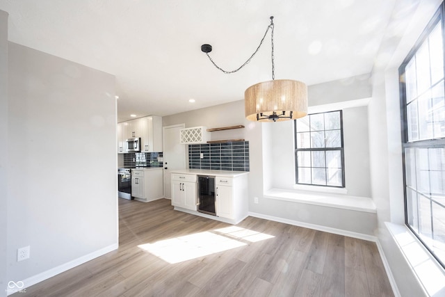 interior space with wine cooler, light wood-style flooring, a chandelier, and baseboards