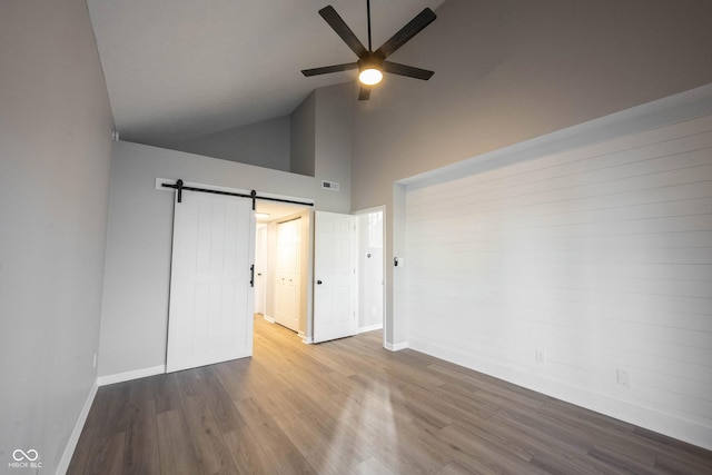 empty room featuring visible vents, baseboards, a barn door, ceiling fan, and wood finished floors
