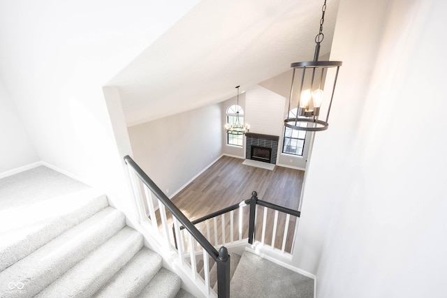 stairway with a fireplace with flush hearth, vaulted ceiling, wood finished floors, baseboards, and a notable chandelier