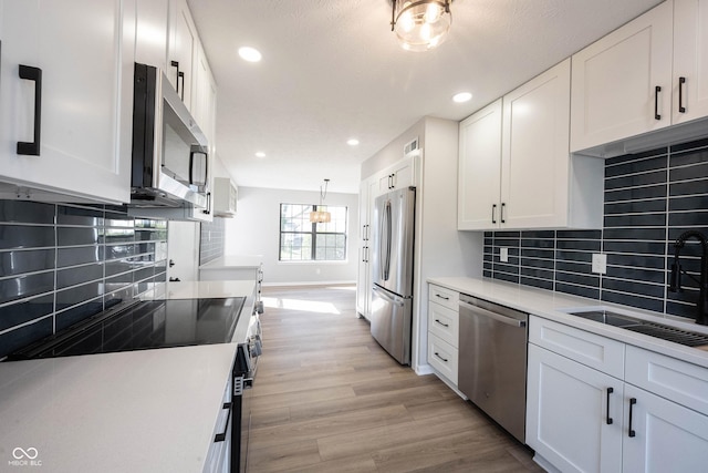 kitchen with baseboards, a sink, light wood-style floors, white cabinetry, and stainless steel appliances