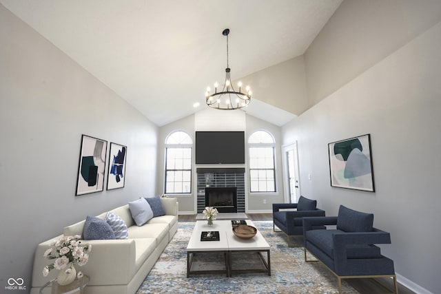 living area with high vaulted ceiling, a tiled fireplace, baseboards, and an inviting chandelier