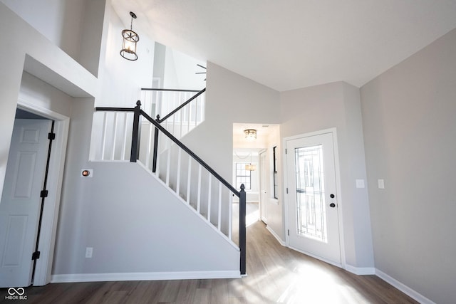 foyer entrance with wood finished floors, high vaulted ceiling, baseboards, and stairway