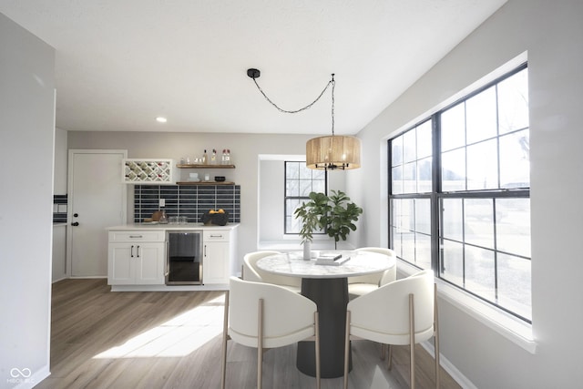 dining space with indoor wet bar, a notable chandelier, baseboards, light wood-type flooring, and beverage cooler
