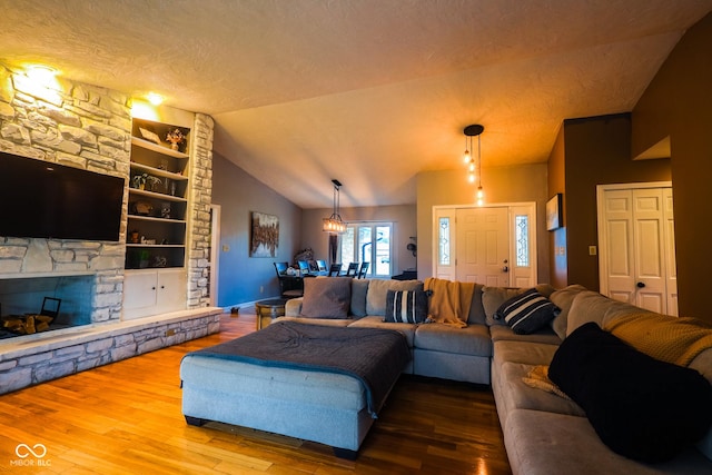 living area with a textured ceiling, wood finished floors, built in shelves, a stone fireplace, and vaulted ceiling