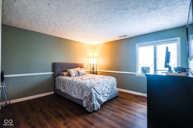 bedroom with baseboards, a textured ceiling, a wainscoted wall, visible vents, and wood finished floors