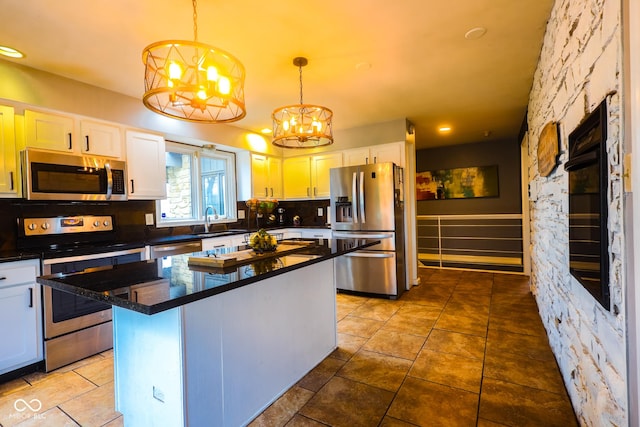 kitchen with dark countertops, appliances with stainless steel finishes, white cabinetry, a sink, and a notable chandelier