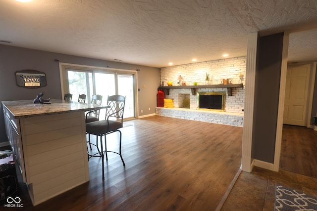 dining area with a brick fireplace, baseboards, dark wood-type flooring, and a textured ceiling