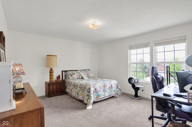 bedroom with light carpet, an office area, and baseboards