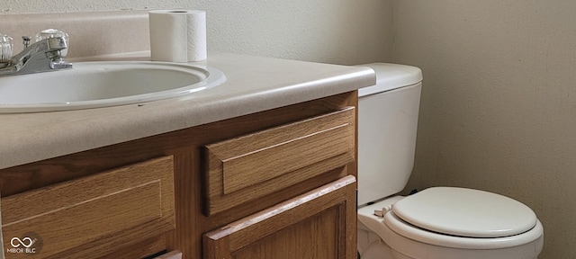 half bathroom with a textured wall, toilet, and vanity