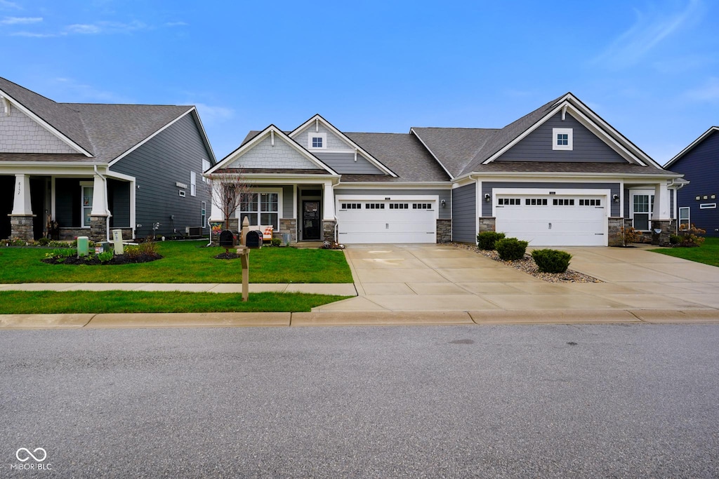 craftsman house with stone siding, an attached garage, concrete driveway, a front lawn, and covered porch