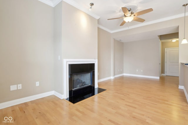 unfurnished living room featuring a fireplace with flush hearth, wood finished floors, baseboards, ceiling fan, and ornamental molding