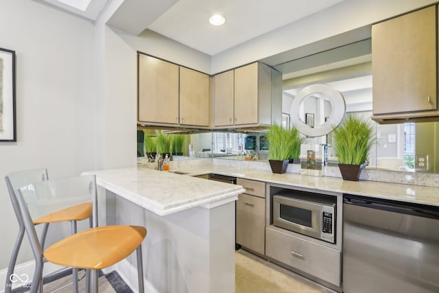 kitchen featuring light stone countertops, a peninsula, a kitchen bar, and stainless steel appliances
