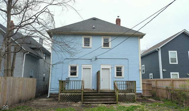 rear view of house with a chimney, roof with shingles, a deck, and fence private yard