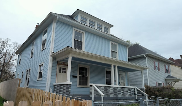 traditional style home with covered porch, a fenced front yard, and a chimney
