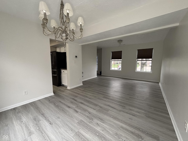 unfurnished living room featuring baseboards, a notable chandelier, wood finished floors, and a textured ceiling
