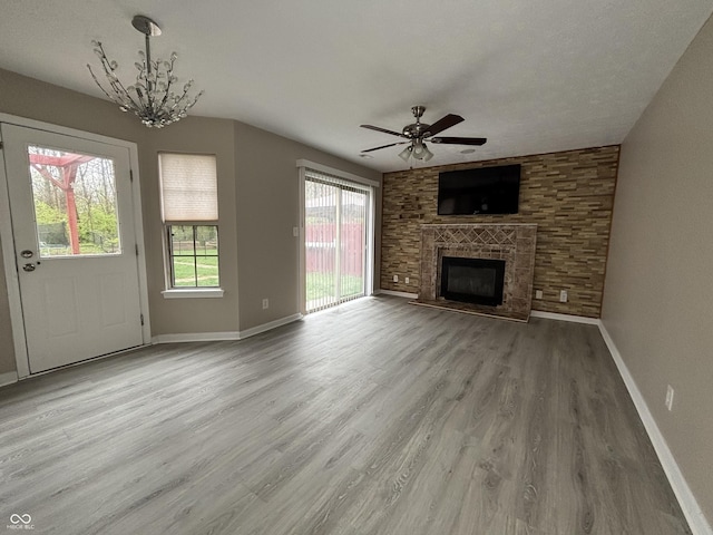 unfurnished living room with ceiling fan with notable chandelier, a fireplace, wood finished floors, and baseboards