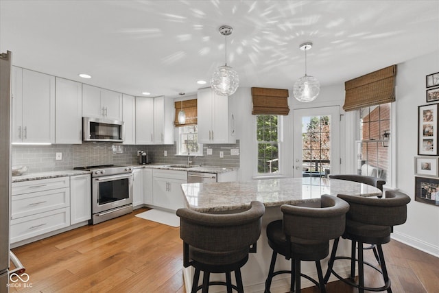 kitchen featuring white cabinets, a sink, light wood-style flooring, stainless steel appliances, and tasteful backsplash