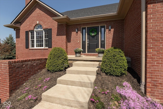 view of exterior entry with brick siding and a shingled roof