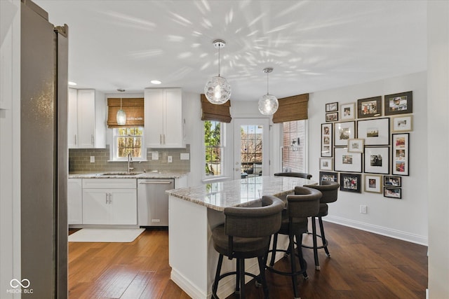 kitchen with appliances with stainless steel finishes, a center island, a sink, white cabinets, and dark wood-type flooring