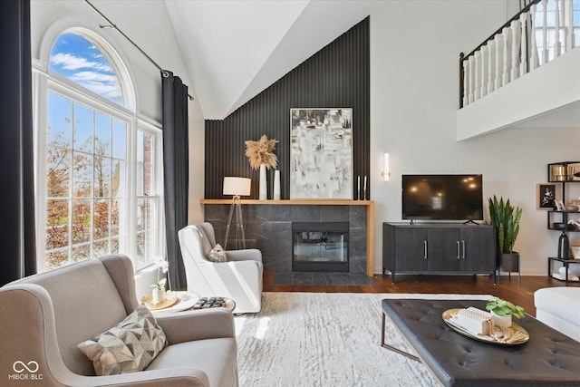 living area with baseboards, high vaulted ceiling, wood finished floors, and a tile fireplace