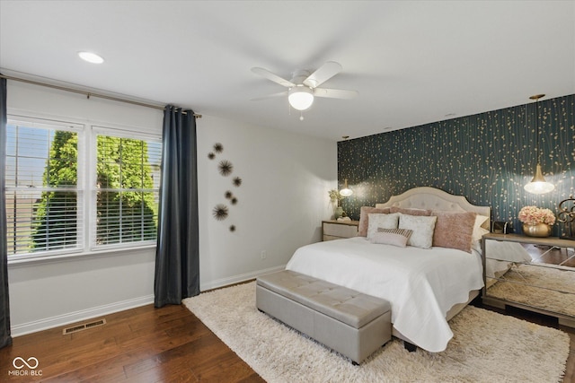 bedroom featuring visible vents, an accent wall, baseboards, wallpapered walls, and hardwood / wood-style flooring