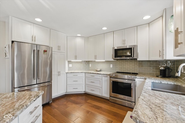 kitchen with a sink, premium appliances, dark wood finished floors, and white cabinetry